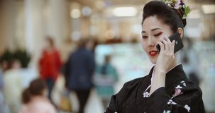 Authentic asian girl in traditional japanese geisha kimono walking in shopping mall or hotel lobby, talking on phone - modern culture concept 4k footage
