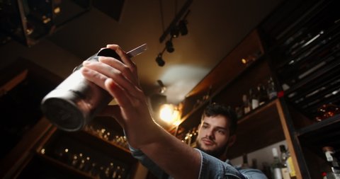 Authentic professional caucasian bartender creating a cocktail drink. Experienced barman pouring alcohol beverage in shaker - food and drink concept close up 4k footage