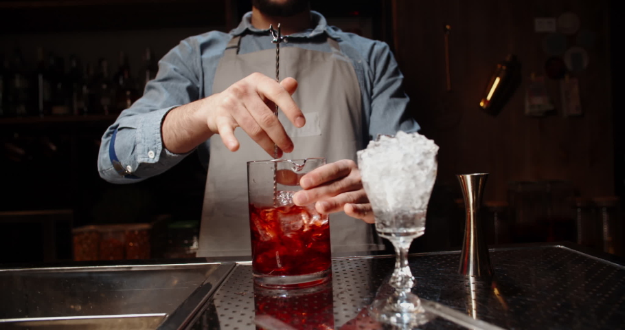 Professional bartender masterly creating a cocktail in modern bar. Experienced barman mixing red alchoholic beverage before serving - food and drink, nightlife close up 4k footage | Shutterstock HD Video #1054550558