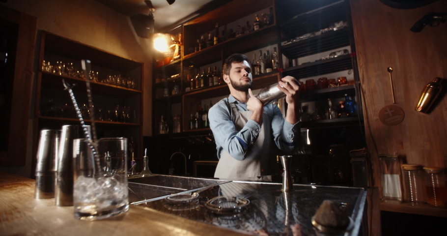 Cool professional caucasian bartender making a cocktail, shaking his shaker. Authentic barman making alcohol beverages in modern bar - food and drink 4k footage Royalty-Free Stock Footage #1054550576