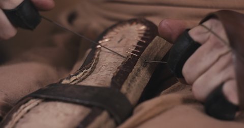 Traditional bespoke shoemaker tightens knot sewing or stitching leather upper to insole on a wooden shoe last with thread gloves on his hands unrecognizable close up slow motion