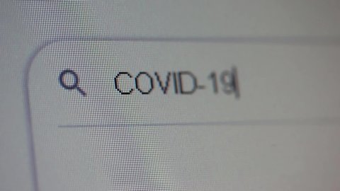 Typing COVID-19 into Search Bar on Computer Monitor. Close Up.