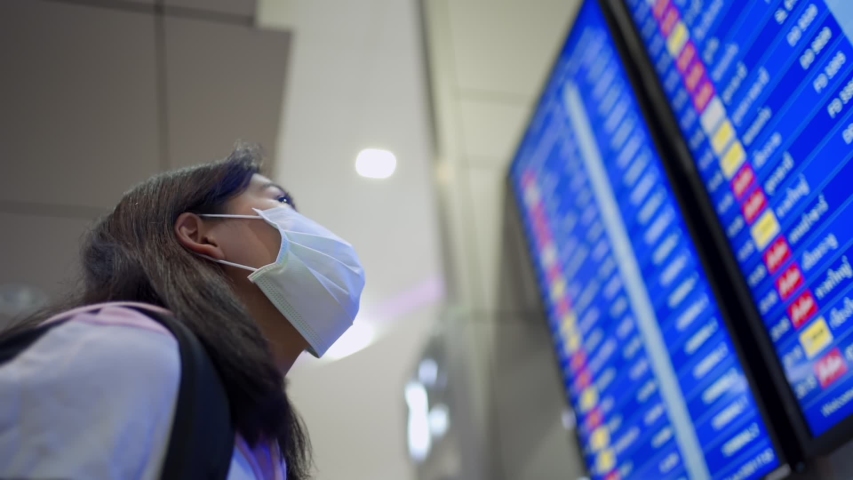 Asian woman looking up at airport schedule time table, wear protective mask, covid-19 pandemic, new normal, flight time schedule, blue led screen, look for check in counter, airport terminal  Royalty-Free Stock Footage #1054560080