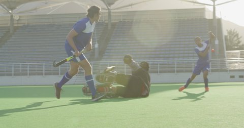 Two multi-ethnic teenage male field hockey teams, playing a field hockey game, with one of the players running through the defense and passing the ball to his teammate, who fails to hit it