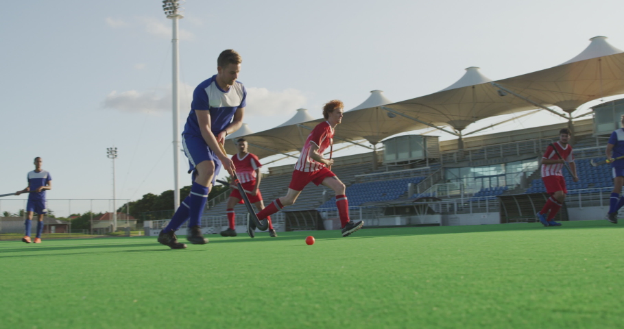Two multi-ethnic teenage male field hockey teams, playing a field hockey game, with one of the players running through the defence and hitting the ball with a hockey stick, which hits a bar Royalty-Free Stock Footage #1054560362