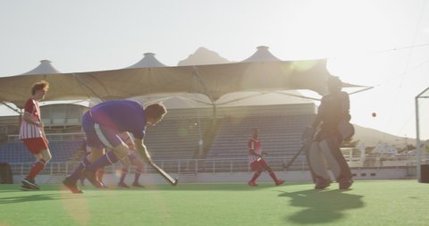 Two multi-ethnic teenage male field hockey teams, playing a field hockey game, with one of the players running through the defence and hitting the ball with a hockey stick, which hits a bar