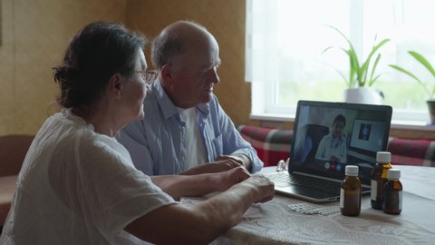 modern medicine, man and woman of retirement age consult doctor online via video link during quarantine pandemic while sitting at home at table with laptop