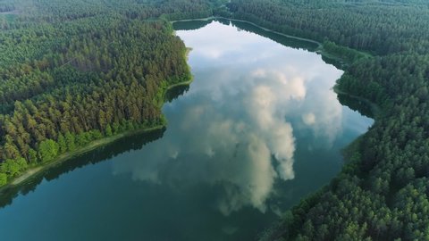 Beautiful landscape in aerial drone shot. Forest woods and calm tranquil lake. Fat white clouds mirroring on water surface.