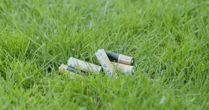 View of used batteries rubbish in the grass. Mans hands put a phone with grass background in front of trash. Virtual image hides real situation from us. Vertical video.