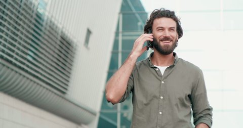 Attractive man with Well groomed Hairstyle and Beard Using his Smartphone outdoor. Having nice and Interesting Appearance. Khaki color Shirt on Handsome man. Speaking on his Mobile phone.