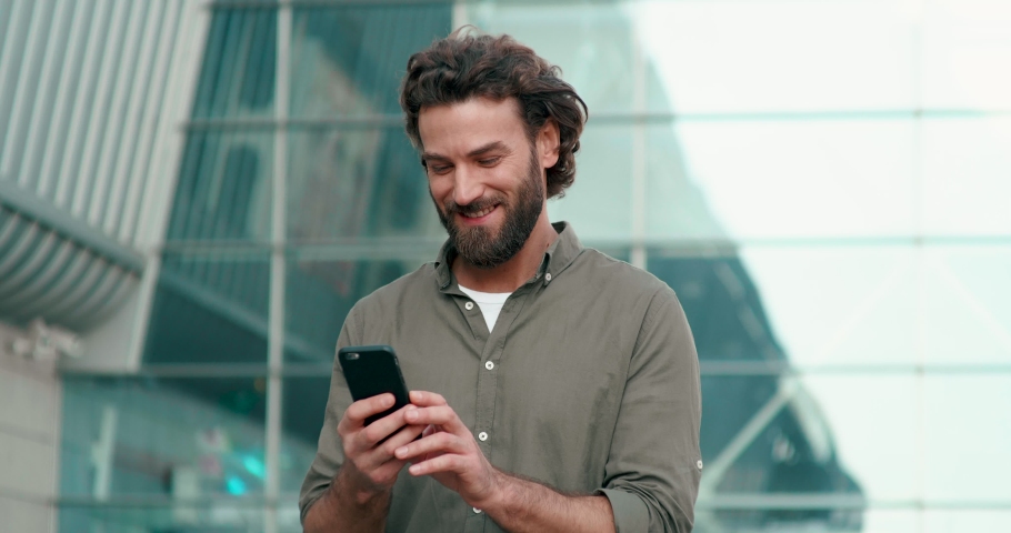 Man in casual outfit Using his Modern Smartphone, walking near Business Center. Man Typing Messages, browsing Mobile Phone and chatting in Social Networks | Shutterstock HD Video #1054569962