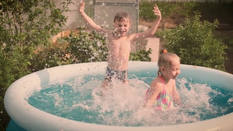 Children bathe and frolic in the pool in the summer, splashing water, lifestyle design. Activity nature leisure. Slow motion.