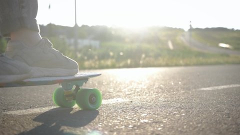 Close up legs riding on skateboard in motion of asphalt at sunset. Youth leisure concept. Active outdoor sport for kids.