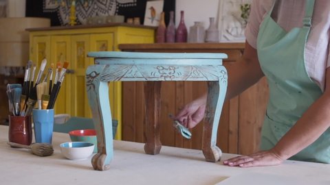 Woman doing home improvement project and painting antique ornate coffee table in carpenter workshop