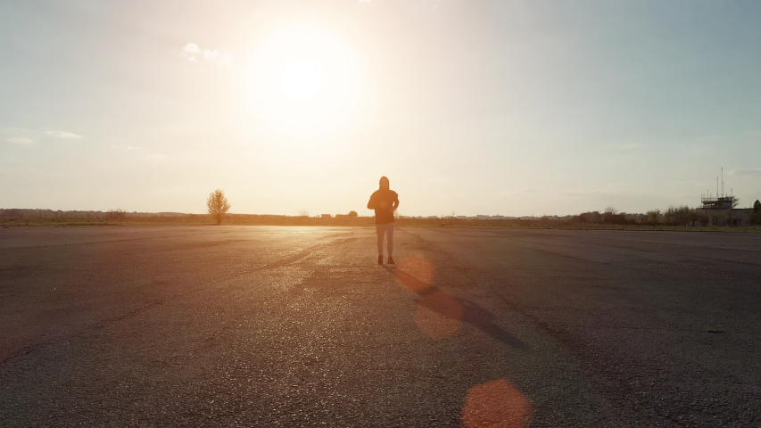 Man in black hood and white pants running outdoors at evening time.