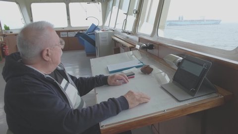 elderly videographer sits in wheelhouse of Natig Aliev tanker against Maersk Line container ship on horizon close view