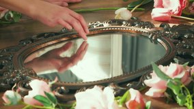 Beautiful womans hand gently touches glass old antique vintage bronze mirror. Mirroring finger display, reflection of arm, room. Backdrop wind blows leaves, petals pink white flowers roses, tulips - Powered by Shutterstock - Get 15% off with code: PIKWIZARD15