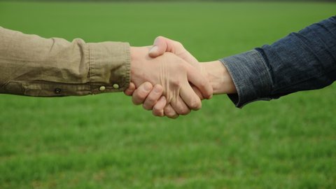 Handshake of two male hands. Two farmers shaking hands against the background of a green wheat field