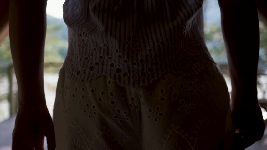 young woman in shorts, a t-shirt and a black hat dancing on a terrace with mountain views. Attractive brunette covers her face with a hat enjoys nature in the mountains