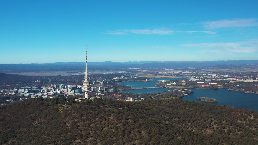 Aerial flyby of Telstra Tower in Canberra, the capital of Australia, showing a panoramic view of Lake Burley Griffin and surrounding landmarks and countryside        Royalty-Free Stock Footage #1054591079