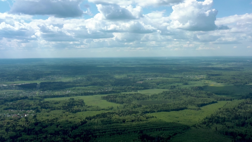 Green russian field under cloudy sky shot from drone. High quality 4k footage of russian green forest under grey cloudy sky in summer, aerial drone shot of russian nature