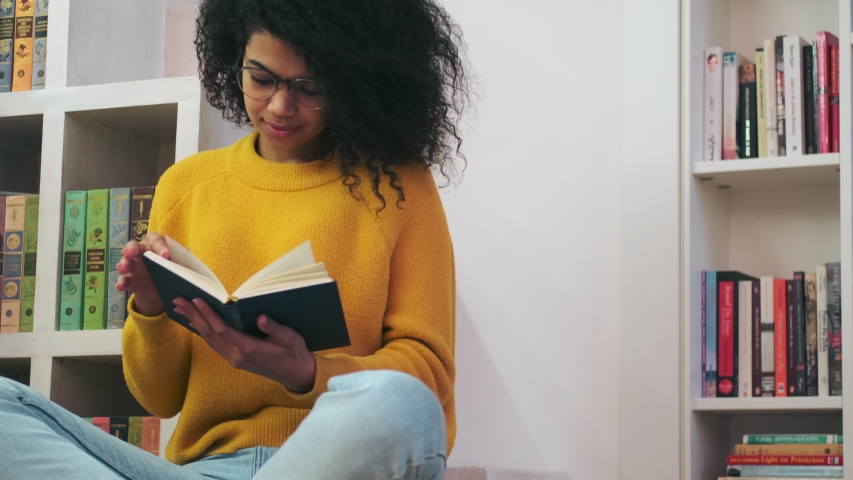 Calm african attractive woman in eyeglasses reading book while sitting on the floor indoors Royalty-Free Stock Footage #1054595162