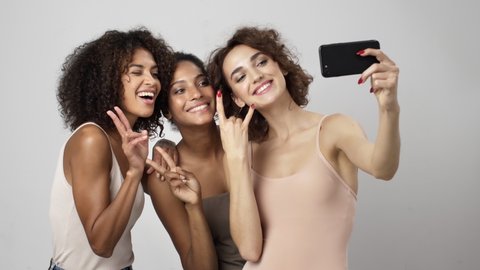Three beautiful multi-ethnic women are taking selfie-photo on the smartphone isolated over white background