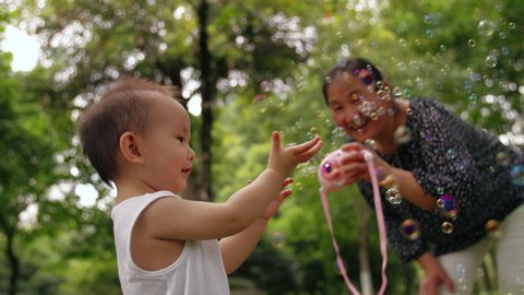 Slow motion of lovely asian baby girl looking at catch soap bubble outdoor in the summer park family lifestyles with kid senior woman playing with her baby granddaughter 4k slow motion footage の動画素材