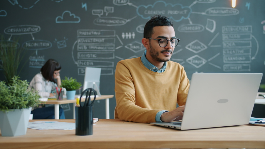 Portrait of Afro-American man working with laptop in open space office typing enjoying job. Coworking, young people and modern technology concept. Royalty-Free Stock Footage #1054600277