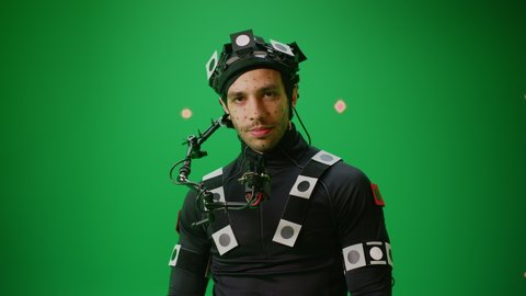 Portrait of an Actor Wearing Motion Caption Suit and Head Rig Posing with Green Screen Background. Studio Big Budget Filmmaking On Film Studio Set Shooting Blockbuster Movie with Chroma Key