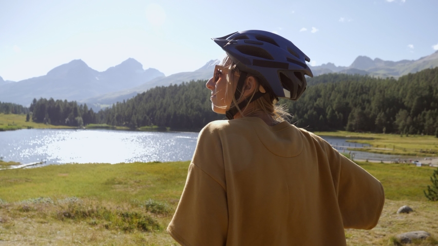 Mountain biker stops by the lake to look at beautiful mountain landscape. Girl on bicycle enjoying outdoor activities in Summer 