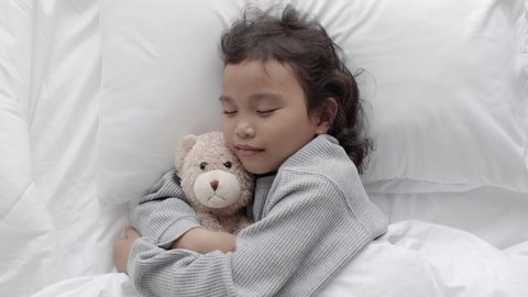 Asian little girl sleeping and hug teddy bear in the bed