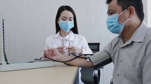 A female doctor wearing a face mask finished measuring the pulse for a middle-aged patient who has a fever and comes to see the doctor at the healthcare center.