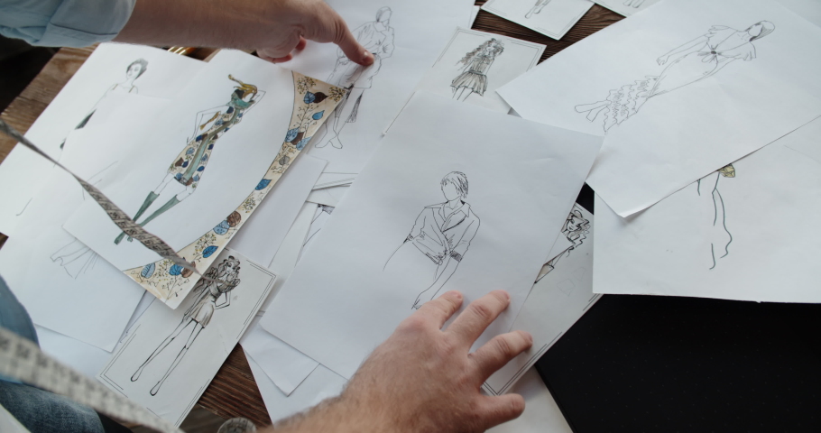 Close-up shot of hands of a clothes designer touching different beutiful sketches of new clothing collection - small business, art concept 4k footage