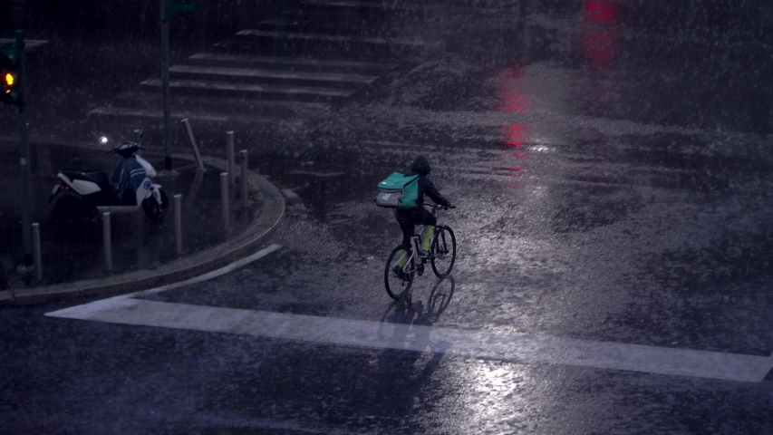 Milan, Italy. Night city in rainy weather. Cars passing on the wet asphalt of city streets. Traffic lights at night. Reflection in puddles on the ground. Crossroads at night. food delivery bike.  Royalty-Free Stock Footage #1054608122