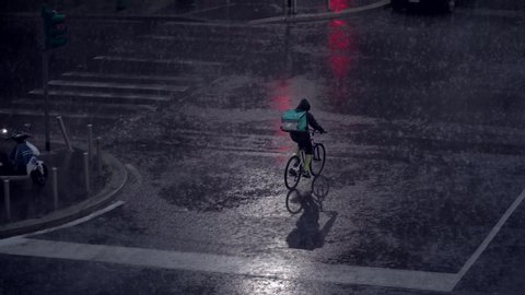 Milan, Italy. Night city in rainy weather. Cars passing on the wet asphalt of city streets. Traffic lights at night. Reflection in puddles on the ground. Crossroads at night. food delivery bike. 