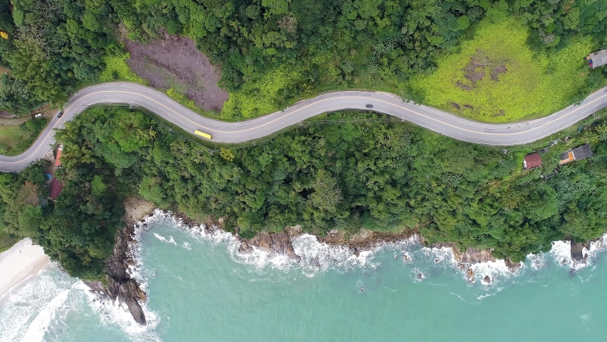 Top down view of curves of coastal road. Highway and freeway road. Beach seascape. Beach life landscape. Brazilian roads. Beach summer scene. Coastal road. Beach scene. Freeway and highway coast road Royalty-Free Stock Footage #1054608419