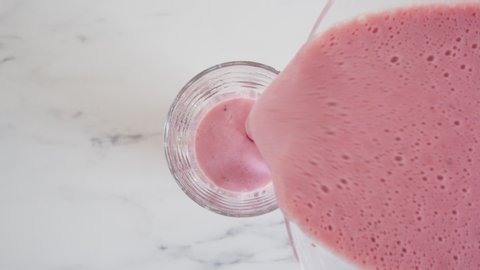 Filling glass cup with strawberry milkshake smoothie, fruit juice with milk is poured into a glass cup, top view close up.