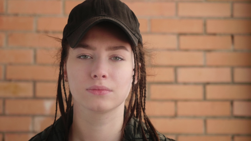 Young caucasian girl looks at camera and amswers the phone. Red bricks wall on the background.