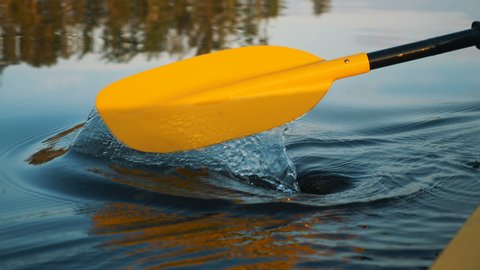 outdoor activities, close-up of a yellow oar rowing on calm water against a background of sunset rays, slow motion