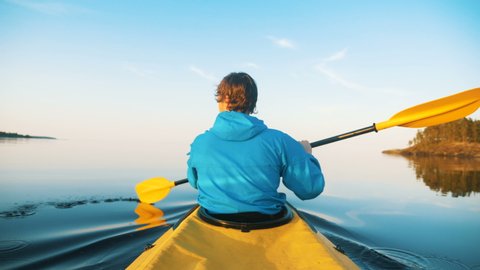 self-isolation in outdoor activities, a man kayaking on a calm lake at sunset: film stockowy