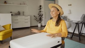 Tilt up side view medium shot of happy senior woman packing luggage for vacations at home. Woman putting on straw hat, closing suitcase and day dreaming - Powered by Shutterstock - Get 15% off with code: PIKWIZARD15