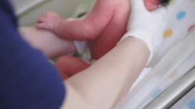 Infancy, childhood, medicine and health, pediatrics concept - close-up shot of female hands in white rubber gloves examining newborn baby with belly button clip in first minutes of life in medical bed