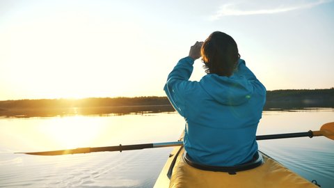 man makes a sunset photo on a smartphone sitting in a kayak on a calm lake, outdoor activities