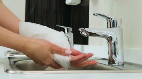 Caucasian woman cleaning her hands with white soft tissue paper on the background of the sink in the dental clinic