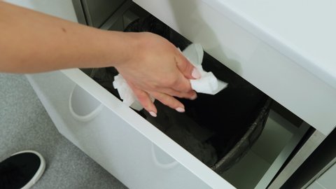 Caucasian woman nurse opens with a knee compartment with a dump and throws a used napkin in the trash in the dental clinic