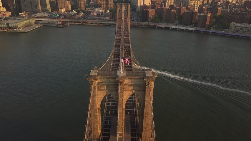 AERIAL: Flight over Brooklyn Bridge with American flag waving and East River view over Manhattan New York City Skyline in beautiful 4K Royalty-Free Stock Footage #1054622822
