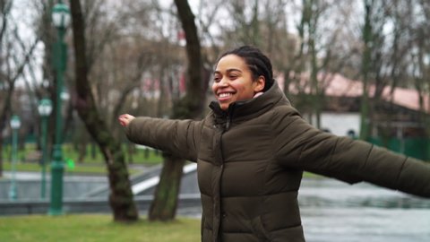 Happy black girl in winter coat spinning and dancing in park