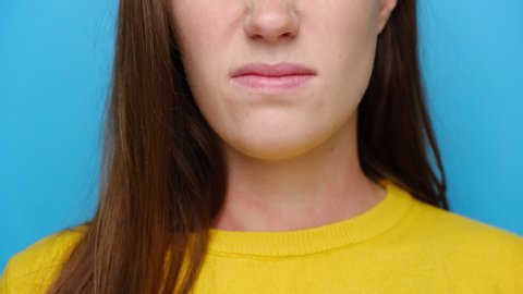 Close up of unhappy young woman squeezing nose with fingers, smells something awful, dressed in yellow sweater, girl feeling bad about bad smell, isolated over blue studio background