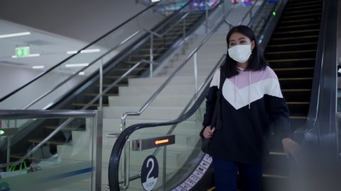Asian woman wear protective mask come down from escalator at the airport travel, covid-19 pandemic, new normal social distance, walk down escalator, indoor building, public social staircase